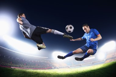 Two soccer players in mid air kicking the soccer ball clipart