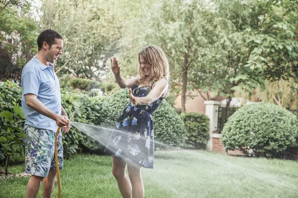 Casal brincando com uma mangueira de jardim — Fotografia de Stock