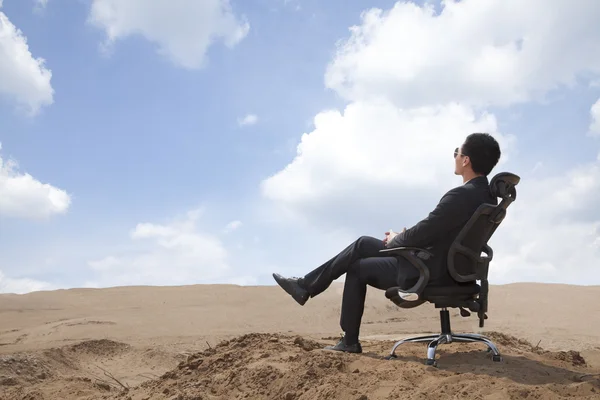 Businessman sitting in an office chair in the desert — Stock Photo, Image