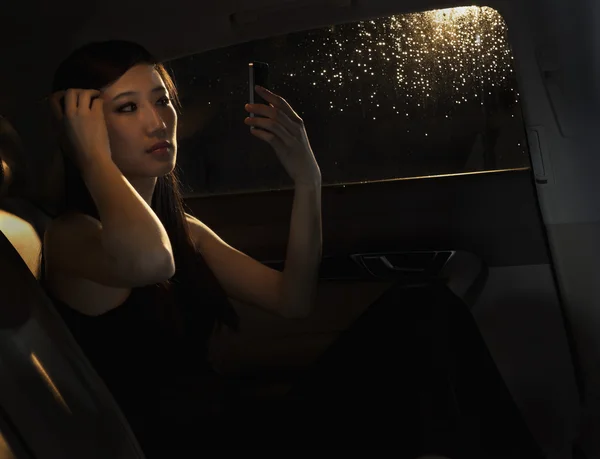 坐在她的车，检查她的头发在电话里的女人 — 图库照片