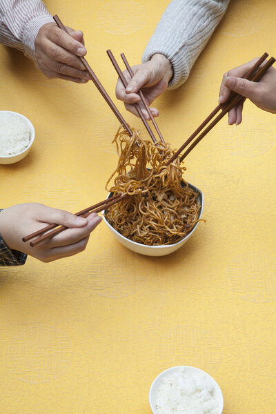 People holding chopsticks and sharing one dish