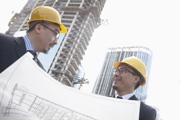 Architects looking at blueprint on construction site — Stock Photo, Image