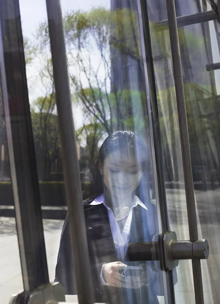 Бизнесмен, использующая телефон по другую сторону стеклянной двери — стоковое фото