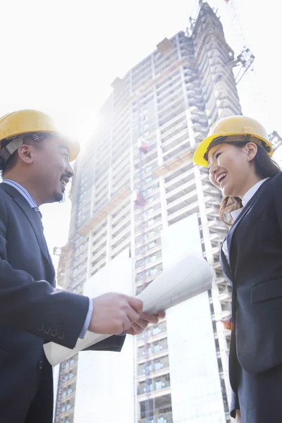 Arquitectos sonriendo en un sitio de construcción sosteniendo el plano —  Fotos de Stock