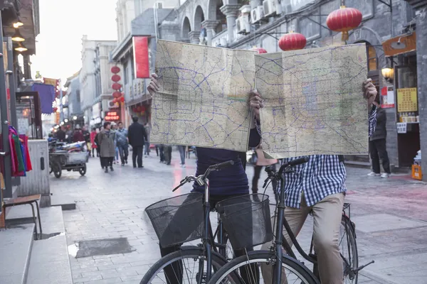 Man and woman on bicycles holding maps — Stock Photo, Image