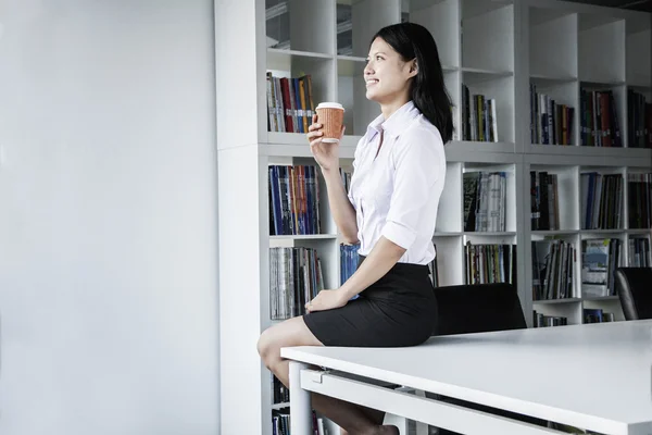 Empresaria sosteniendo un café y sentada en una mesa —  Fotos de Stock