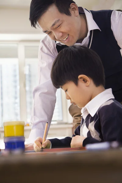 Teacher helping schoolboy with arts and crafts — Stock Photo, Image