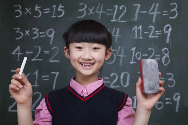 Schoolgirl in front of blackboard holding chalk and eraser — Stock Photo, Image