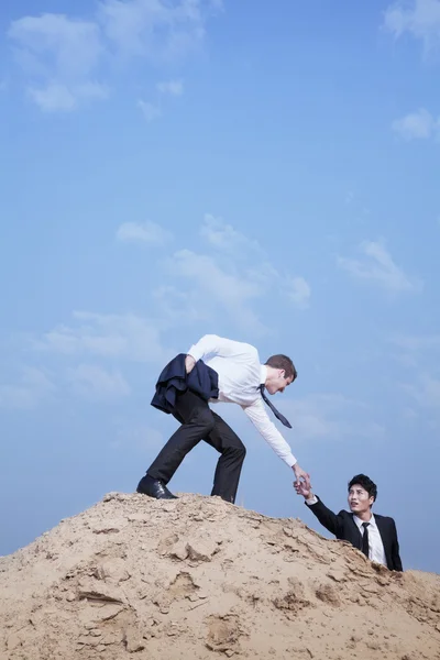 Geschäftsmann hilft einem anderen Geschäftsmann, an die Spitze des Hil zu gelangen — Stockfoto