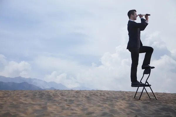Empresário em pé em uma cadeira e olhando através de um telescópio — Fotografia de Stock