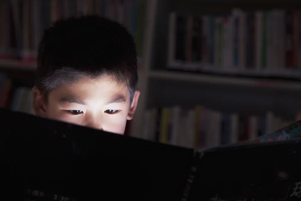 Schooljongen lezen van een boek met zijn gezicht verlicht — Stockfoto