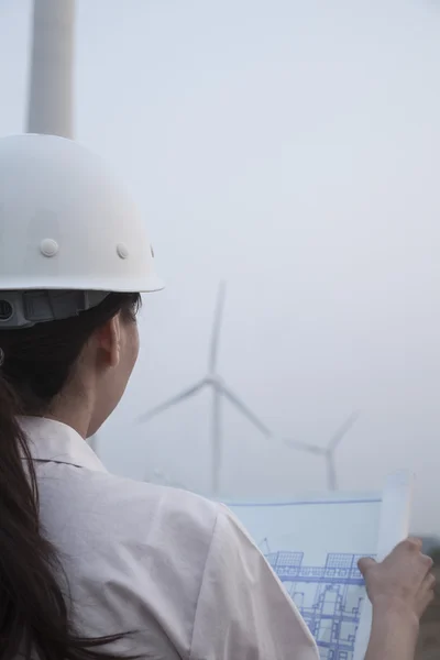 Engineer looking at blueprint with wind turbines in front — Stock Photo, Image