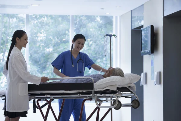 Female doctor and nurse wheeling a stretcher with a patient — Stock Photo, Image