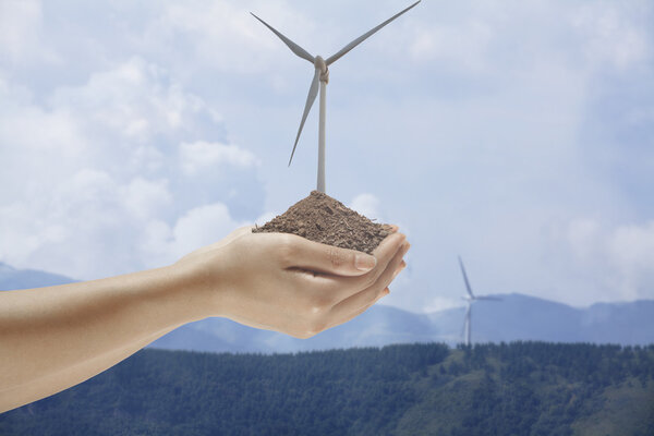 Hands holding soil with a wind turbine
