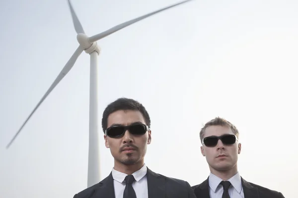 Businessmen in sunglasses standing by a wind turbine — Stock Photo, Image