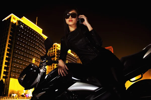 Woman talking on the phone and leaning on her motorcycle at night — Stock Photo, Image