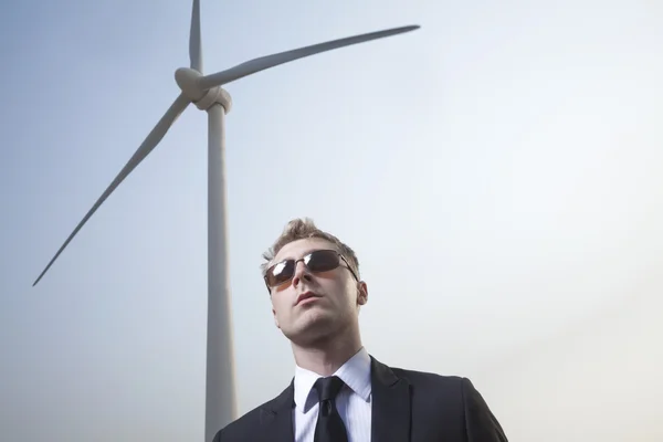 Businessman in sunglasses standing by a wind turbine — Stock Photo, Image