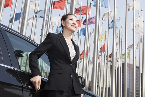 Businesswoman standing near car with flagpoles — Stock Photo, Image