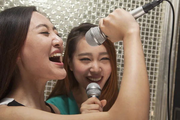 Female friends singing into a microphone at karaoke — Stock Photo, Image