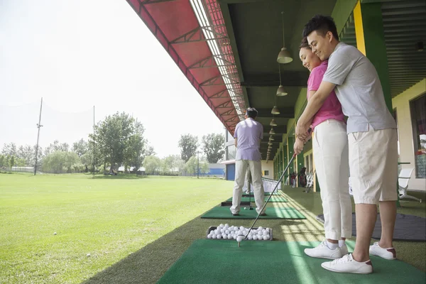 Hombre enseñando a su novia cómo golpear pelotas de golf —  Fotos de Stock