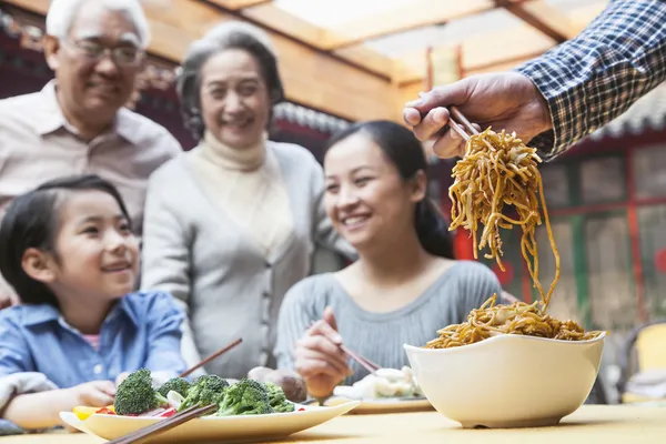 Father serving noodles with chopsticks at a family dinner — Stock Photo, Image