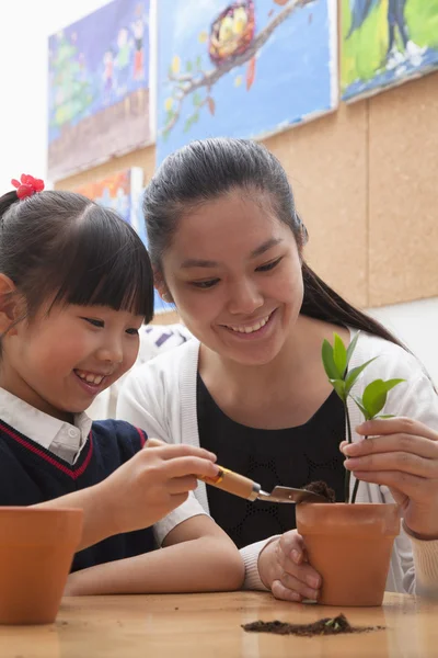 Teacher and schoolgirl planting plants into flowerpots — Stock Photo, Image