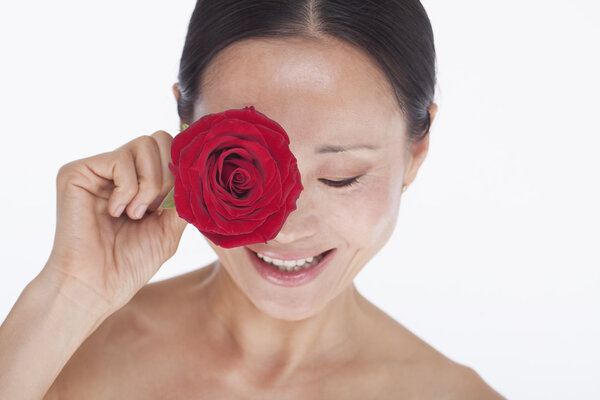 Woman holding a red rose to her eye