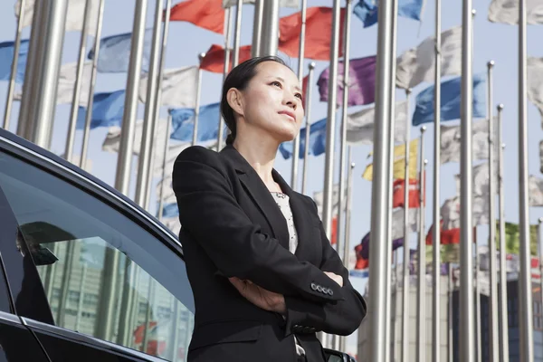 Businesswoman standing near car with flagpoles — Stock Photo, Image