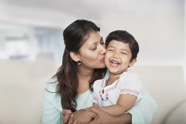 Mãe segurando e beijando sua filha no sofá — Fotografia de Stock