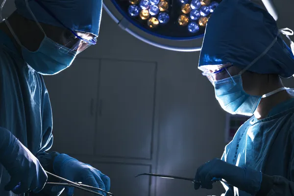 Two surgeons looking down and working at the operating table — Stock Photo, Image