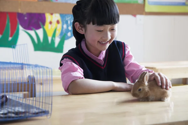 Colegiala acariciando conejo mascota en el aula — Foto de Stock