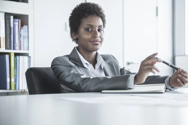 Businesswoman sitting at a table and holding a pen — Stock Photo, Image