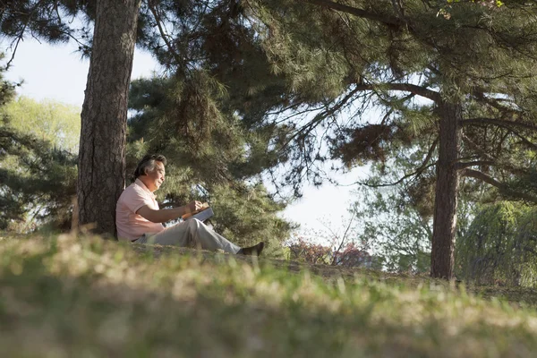 Uomo anziano che legge un libro in un parco — Foto Stock