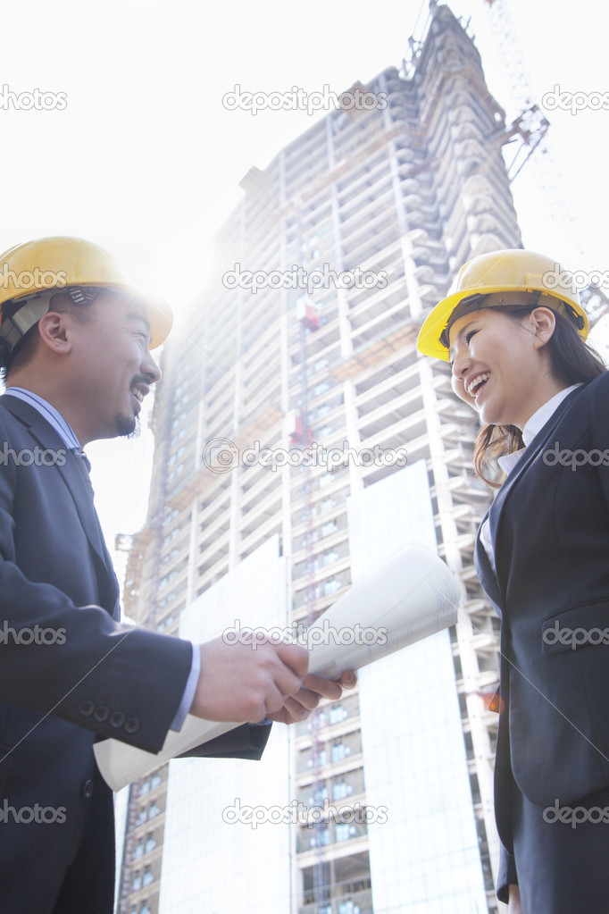 Architects smiling at a construction site holding blueprint