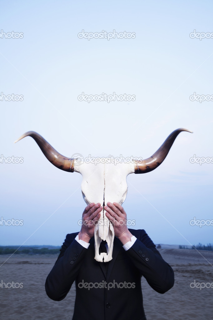 Businessman holding an animal skull in front of his face