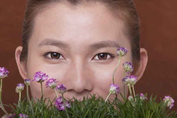 Vrouw met haar gezicht achter sommige bloemen en gras — Stockfoto