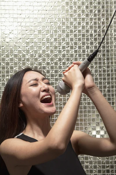 Woman singing into a microphone at karaoke — Stock Photo, Image