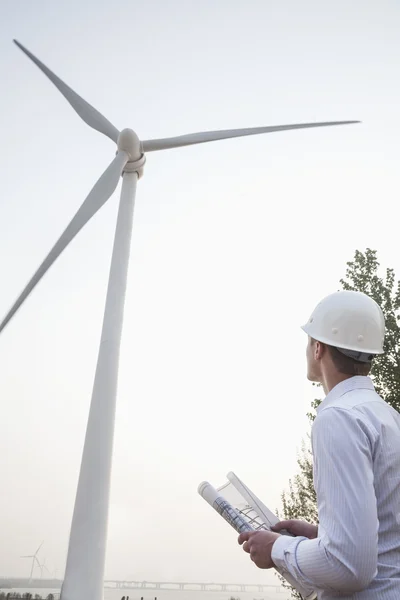 Engineer in a hardhat looking up at a wind turbine — Stock Photo, Image