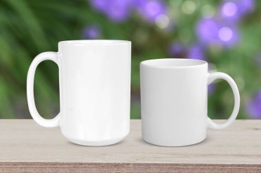 11 oz coffee cup and 15 oz coffee cup relaxing on a rustic light wood tabletop with a pretty floral garden in the background.
