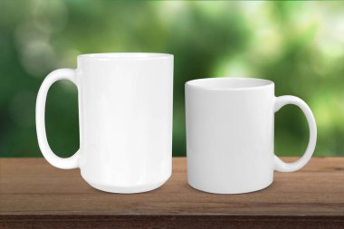 11 and 15 oz. white coffee mugs chilling on a rustic wood tabletop with soft green trees in the background.