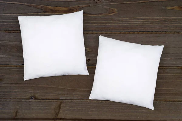 Two white throw pillows resting atop a rustic brown wooden background.