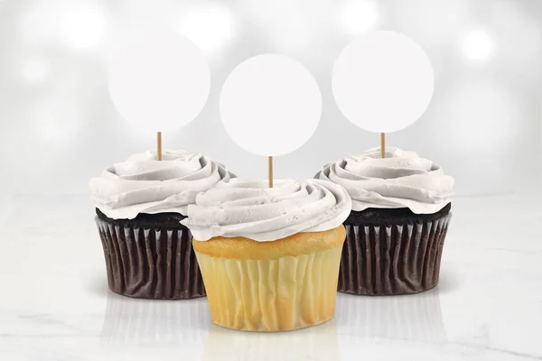 Three classic white frosted cupcakes chilling atop an elegant marble tabletop surrounded by glowing white lights.