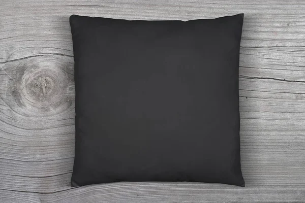 Black throw pillow napping on a weathered gray wood surface.