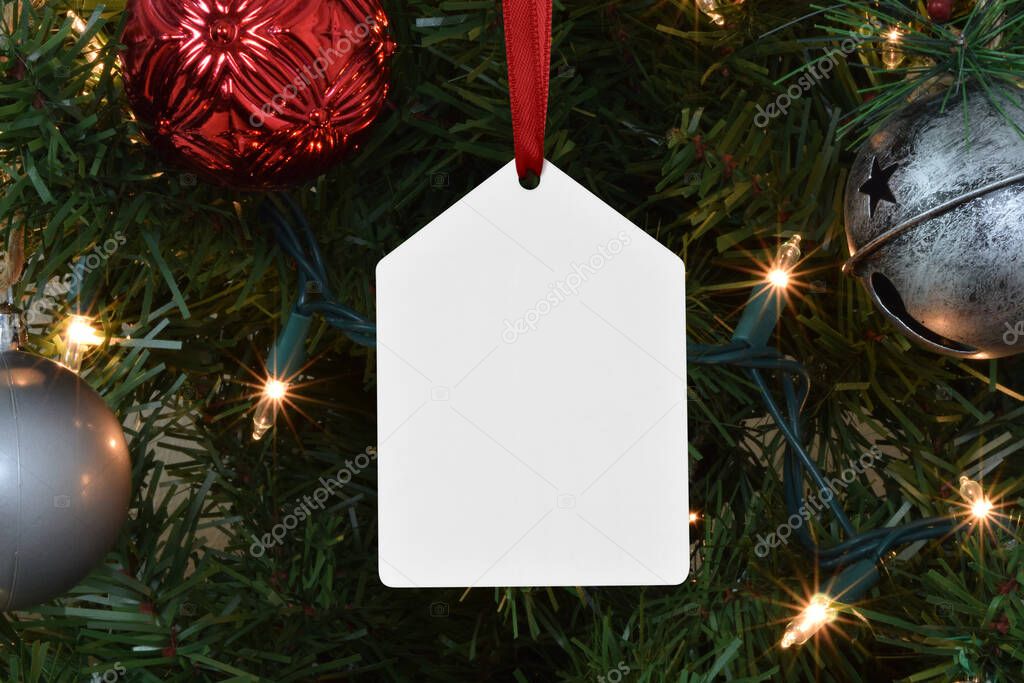 A Christmas Tag Shaped Ornament Dangles Eloquently from a Lit up Christmas Tree. 