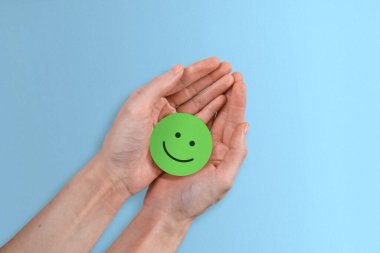 Kadının ellerinde, güzel mavi bir arka planda, pozitif yeşil bir gülen yüz..