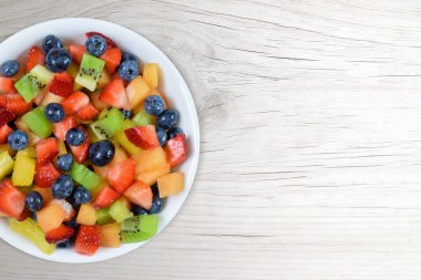 Modern beyaz ahşap arka planda renkli taze meyve salatasının üst görüntüsü. Kopyalama alanı çok.