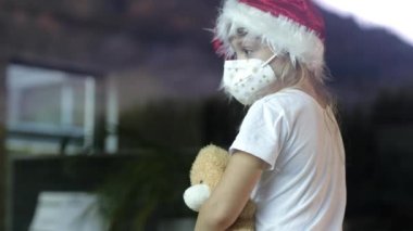 Altı yaşında Noel Baba şapkalı bir kız masada oyuncak ayıyla oturuyor..