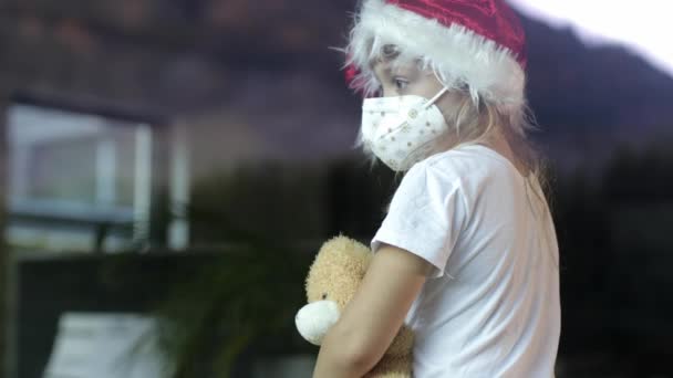 6岁的女孩戴着圣诞老人的帽子和泰迪熊单独坐在桌子上 — 图库视频影像