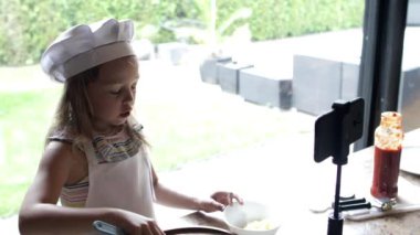 Küçük kız pizza pişiriyor ve akıllı telefonda video blogu için video çekiyor.