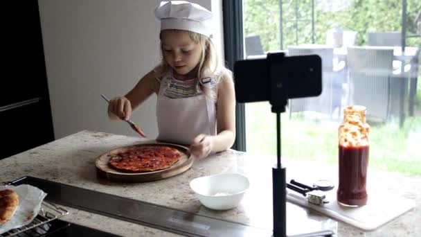 小女孩做饭比萨饼 在家里厨房用智能手机为视频博客拍摄视频 — 图库视频影像